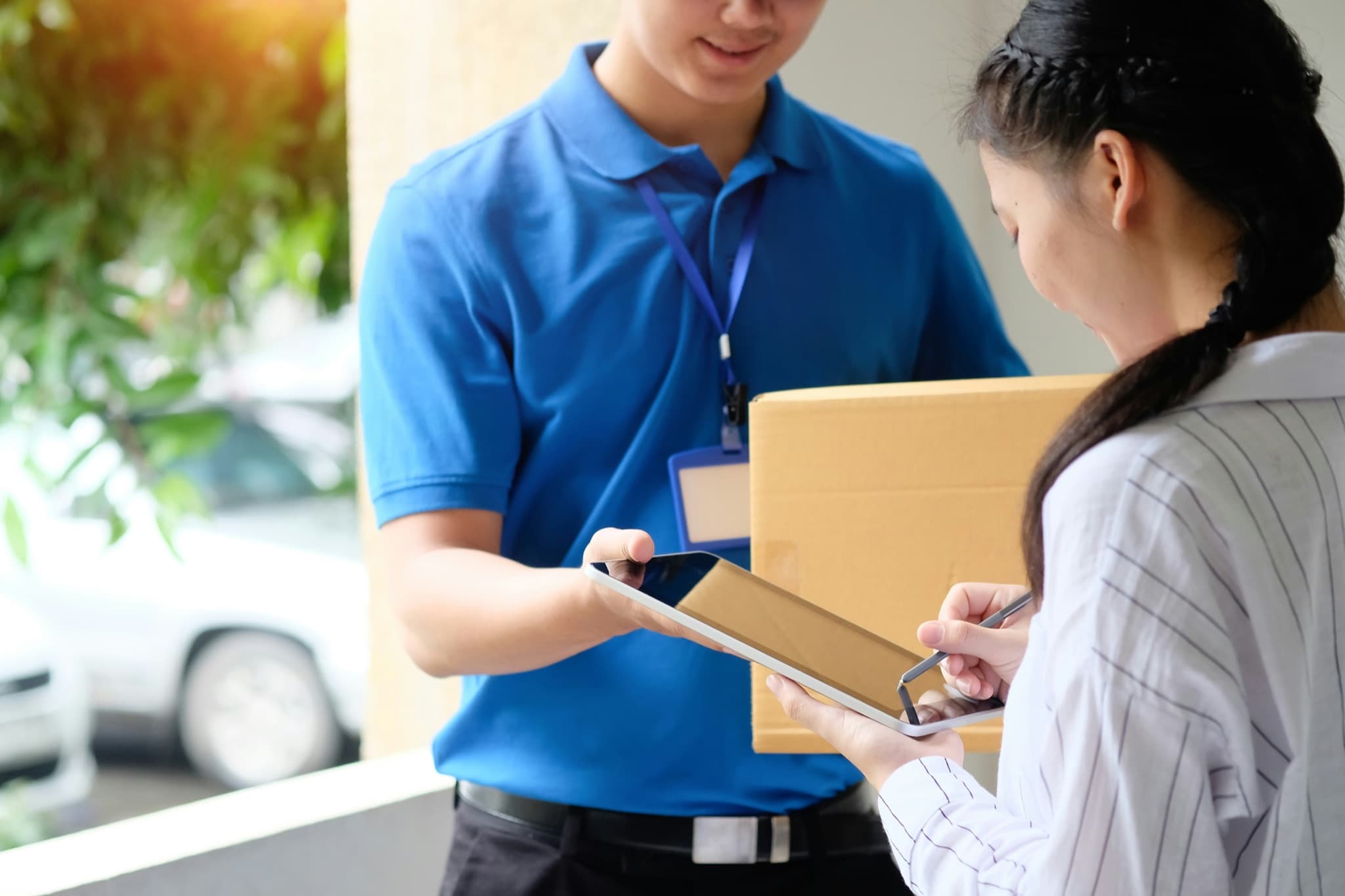 Courier handing a parcel to a recipient who signs for delivery on a tablet